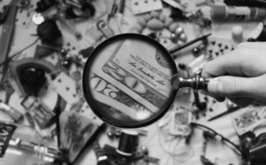 This image of a magnifying glass hovering over cash and goods highlights this post's topic: a fake shop finder.
