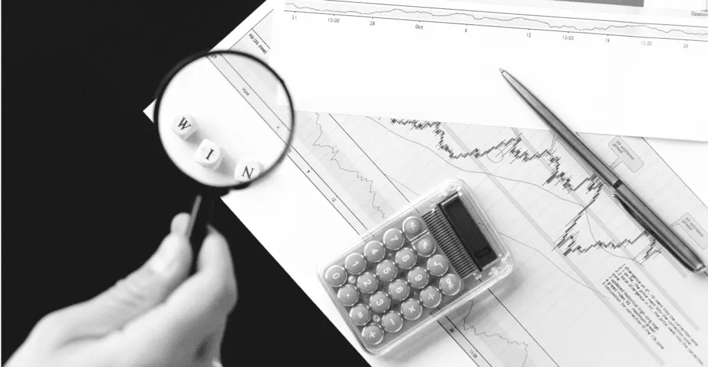 This image of a magnifying glass highlighting charts, a calculator, and some tiles reading "win" highlights our discussion topic: New gTLDs and how businesses prepare for a successful DotBrand strategy.