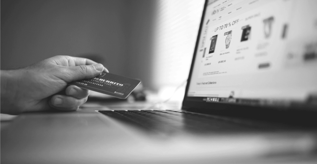 This image of a hand holding a credit card at a computer screen with deals on it illustrates our discussion topic: fake shops online.