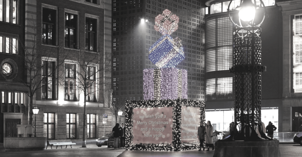 This image of a large sculpture of christmas gifts stacked on top of each other, with festive messages underneath in English and Dutch in central Amsterdam highlights our discussion topic: How different cultures around the world celebrate the festive winter season.