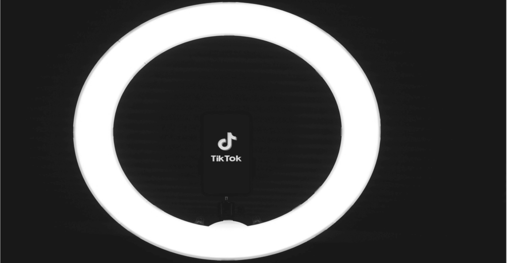 Deze afbeelding van het TikTok-logo op een telefoon in het midden van een licht onderstreept ons discussieonderwerp: TikTok Shop en de bedreigingen die het platform vormt voor merken op het gebied van merkinbreuken, namaakproducten en e-commerce-omzet.