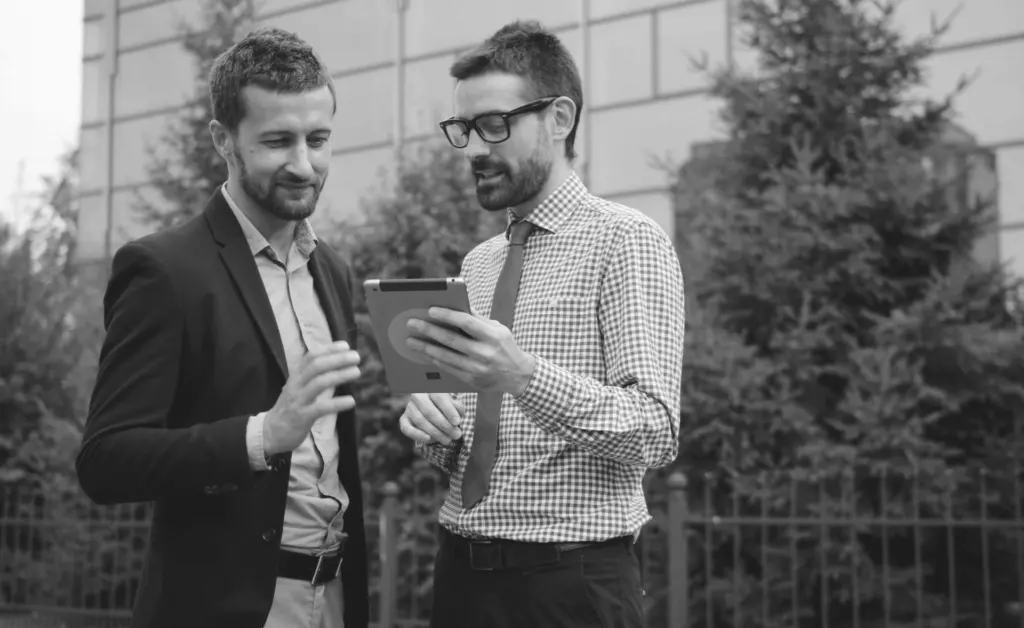 This image of a two smiling colleagues in front of some trees, comparing what they can see on a phone illustrates our discussion topic: scams on Linktree and how to fight back.