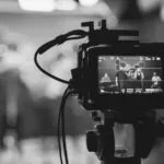 This image of a camera in the foreground and a livestream set in the background illustrates our discussion topic on livestream counterfeiting and how brands can stay safe.