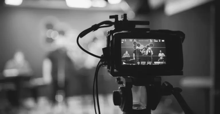 This image of a camera in the foreground and a livestream set in the background illustrates our discussion topic on livestream counterfeiting and how brands can stay safe.